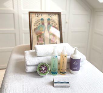 A white massage table with white towels and bottles of reflexology treatment lotions.